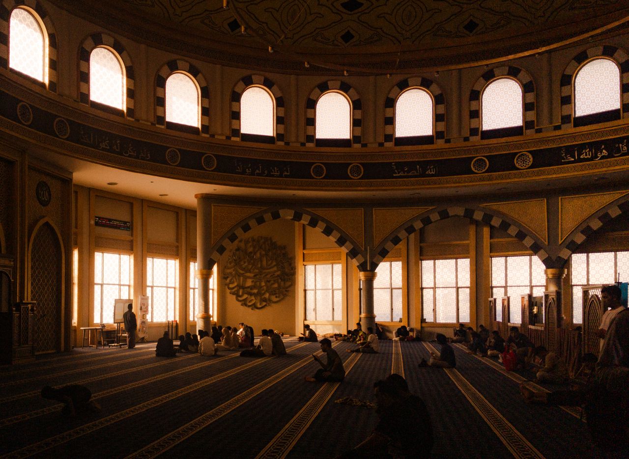 People gathered in a spacious, beautifully lit mosque interior, engaging in various activities.